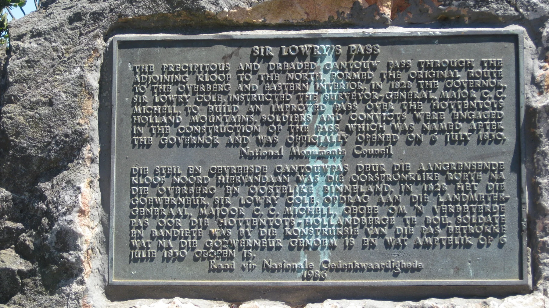 A dark historical plaque is mounted in a rough rock surface.