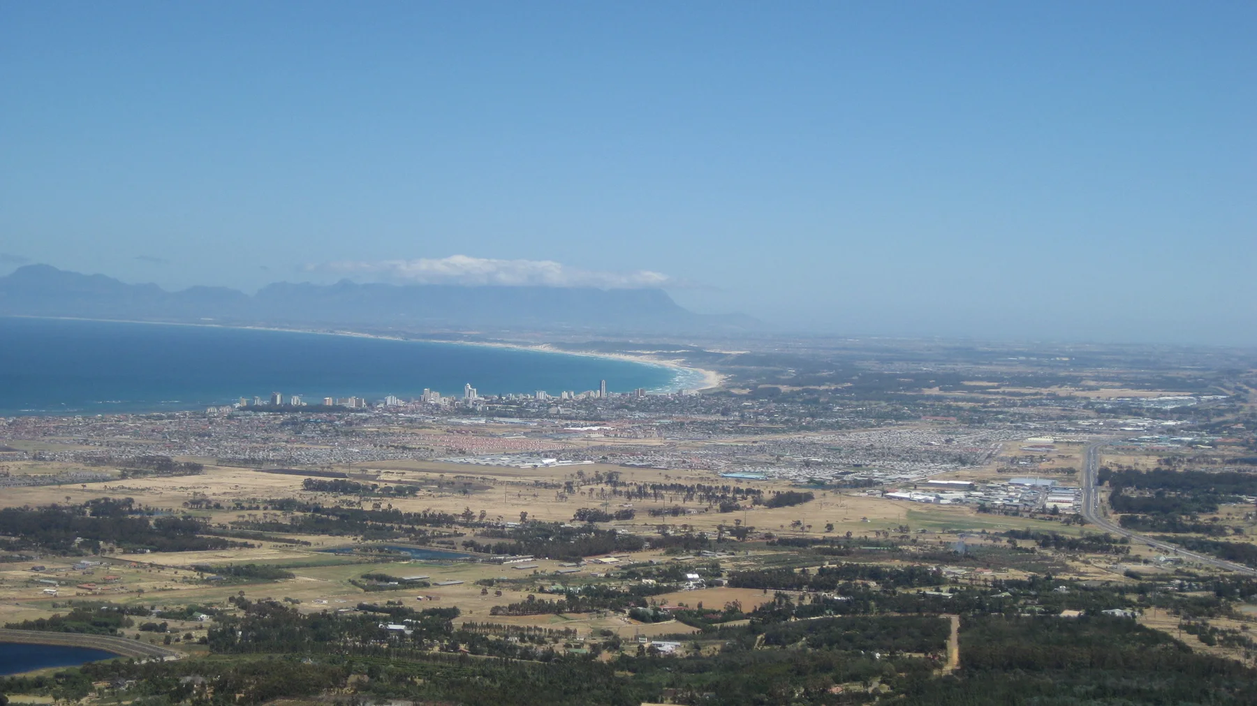 A broad bay curves beyond fields and dense low development.