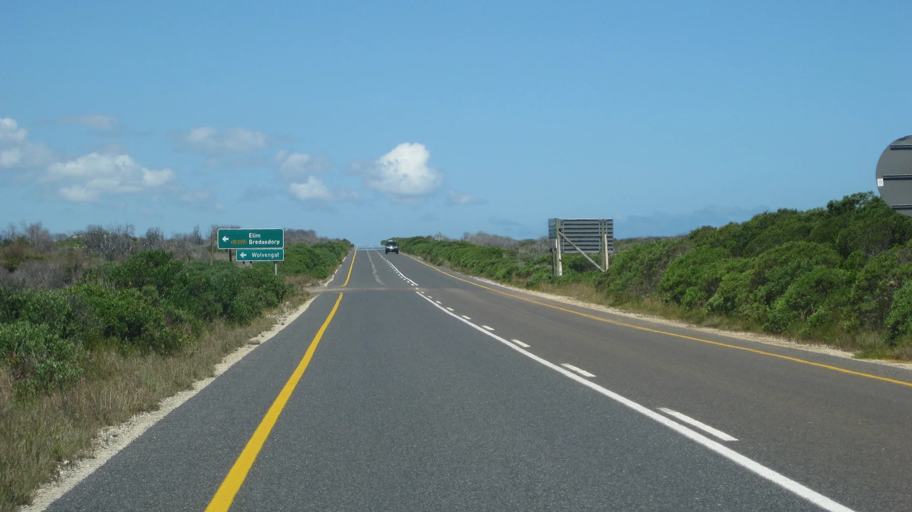 A paved road passes direction signs across low scrubland.