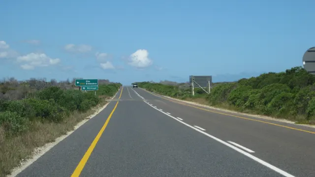 A paved road passes direction signs across low scrubland.