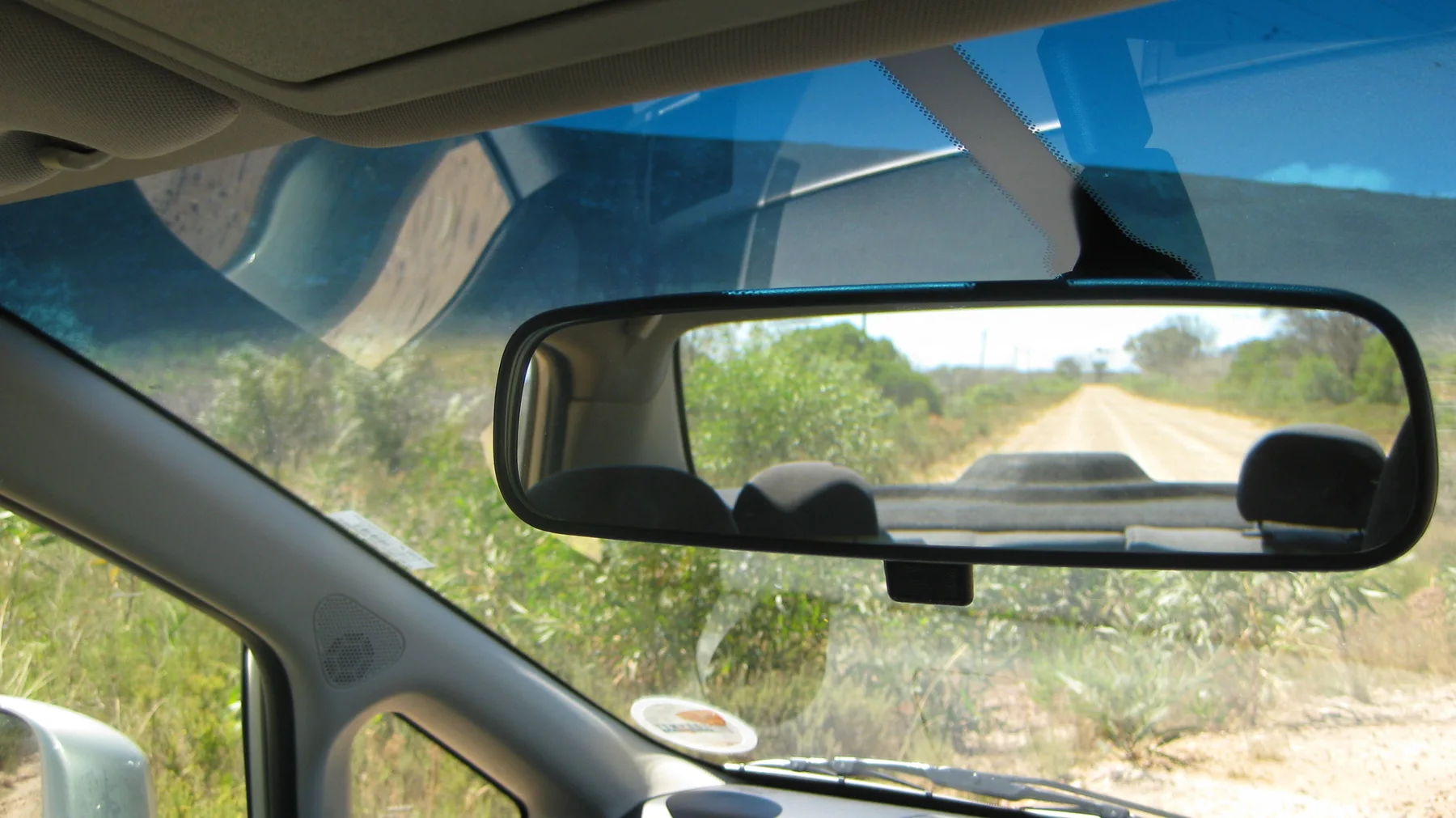 A rearview mirror reflects a dirt road behind the vehicle.