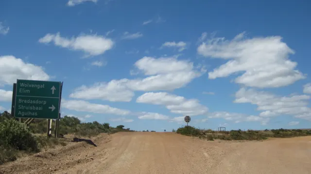 A direction sign stands beside a fork in a dusty road.