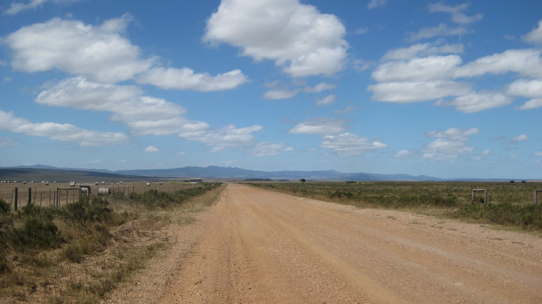 A straight dirt road crosses open land toward distant hills.