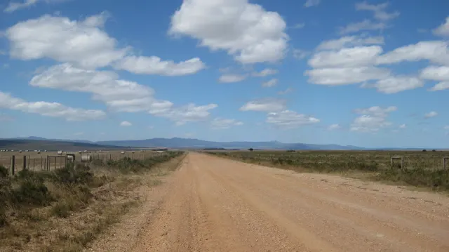 A straight dirt road crosses open land toward distant hills.