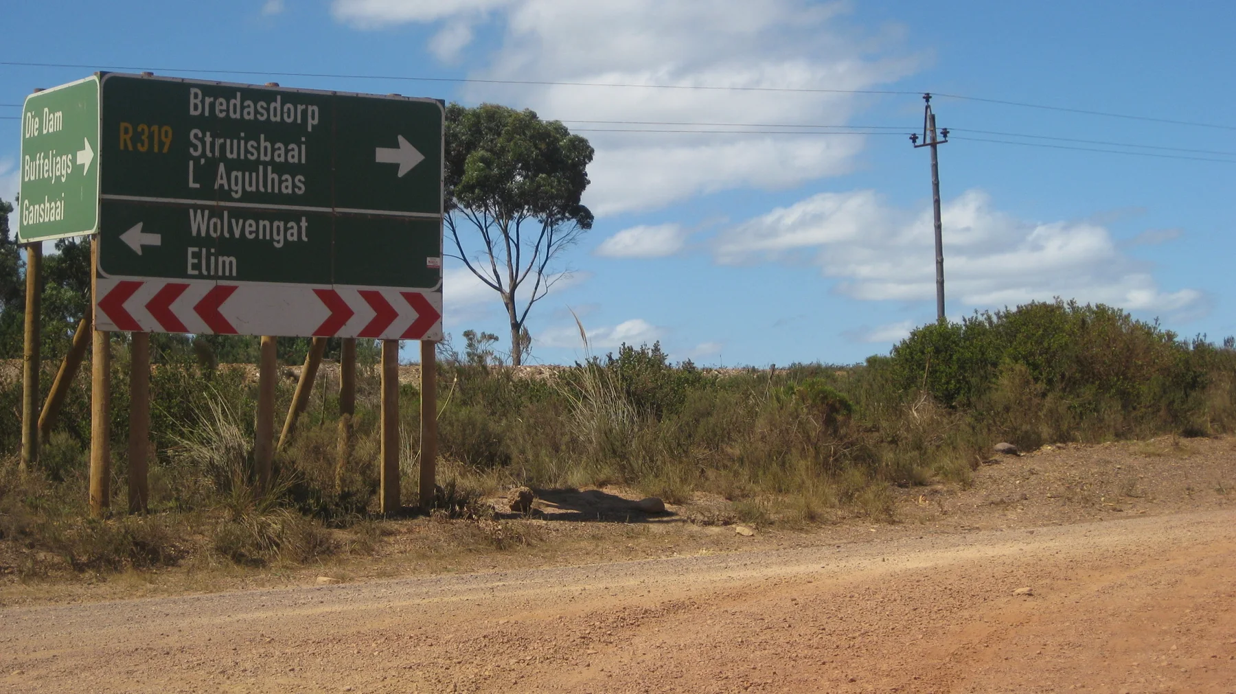 A multi-direction sign marks a dirt junction beside utility poles.