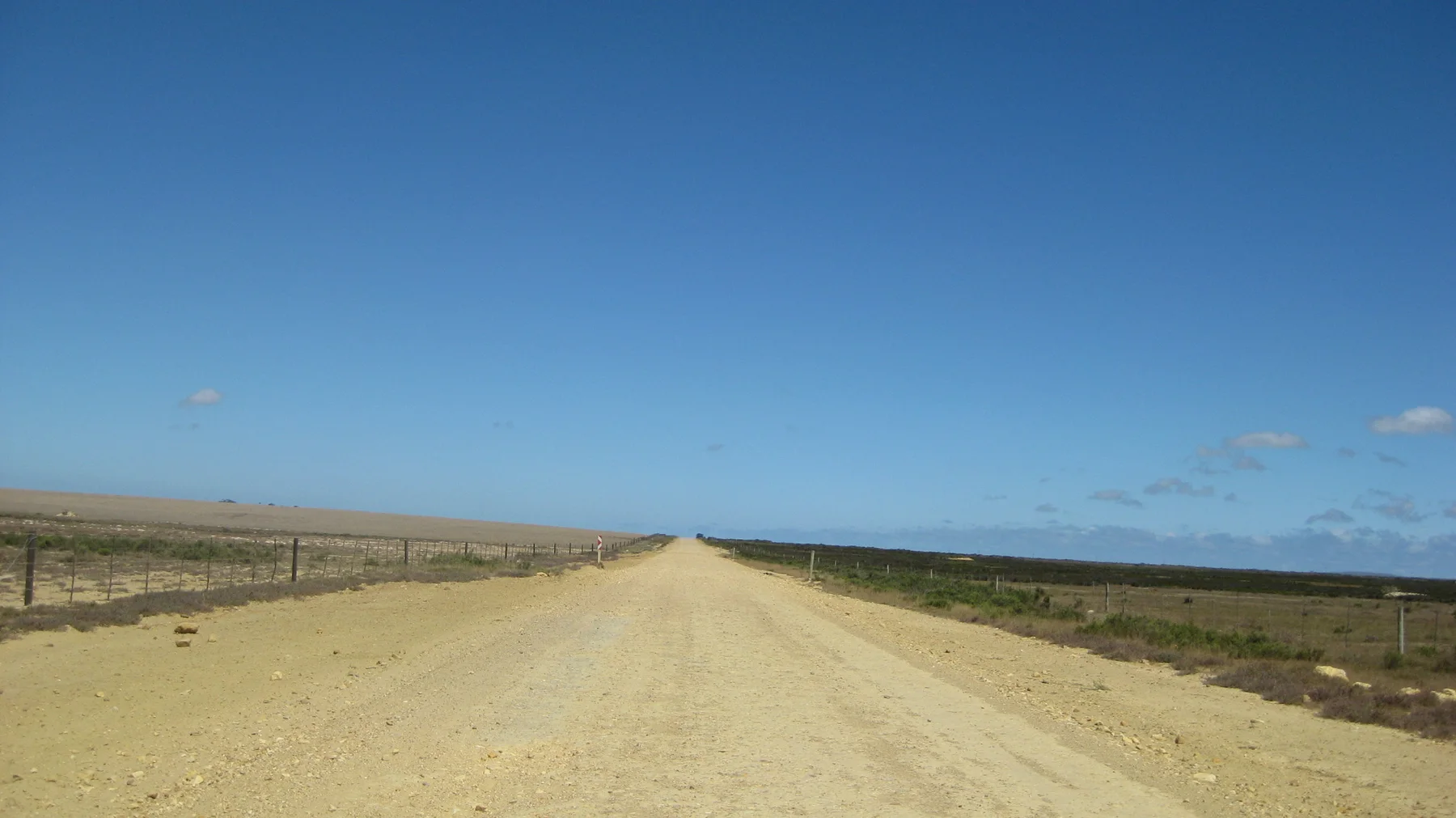 A pale straight road crosses dry open countryside.