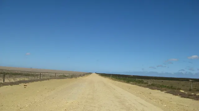 A pale straight road crosses dry open countryside.