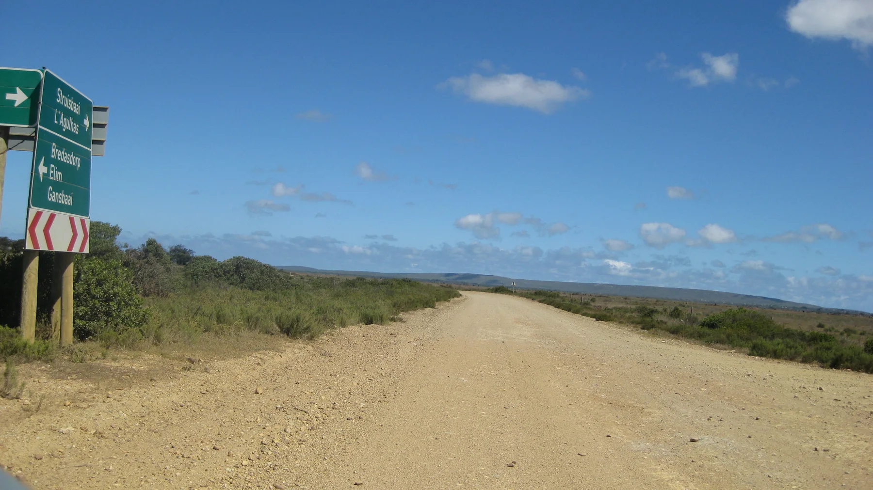 A pale dirt road continues beyond a roadside direction sign.