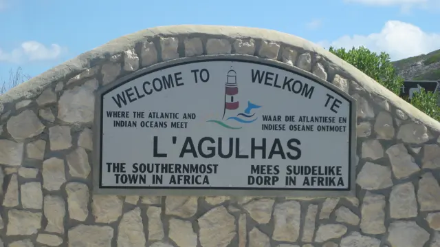 A welcome sign is mounted in a curved stone wall at L'Agulhas.