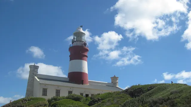 A striped lighthouse stands behind a low white building.