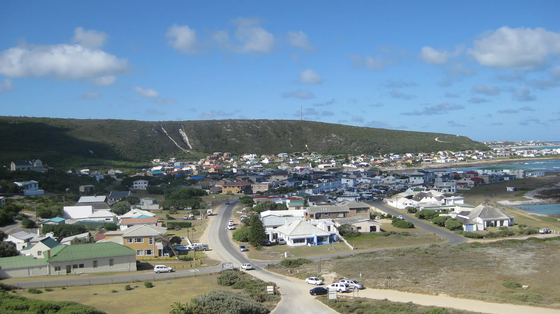 Small houses and curving roads fill a coastal town below.