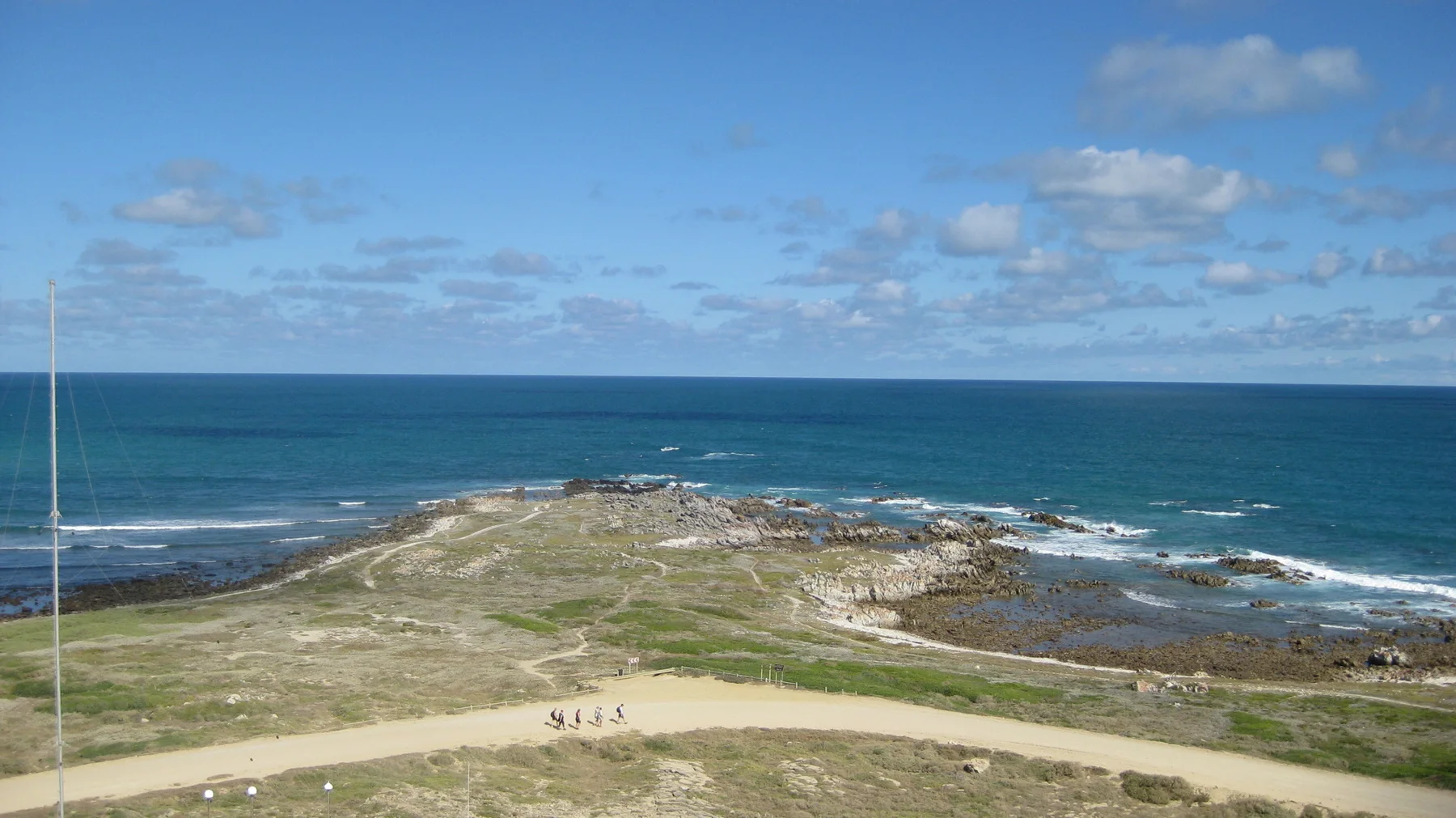 A rocky point projects into blue water beyond a pale track.