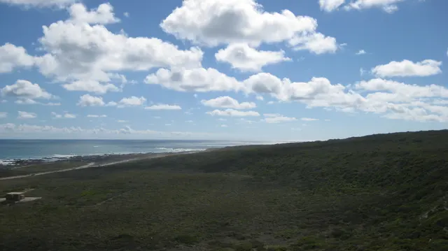 A green rise leads toward a long coastline under white clouds.
