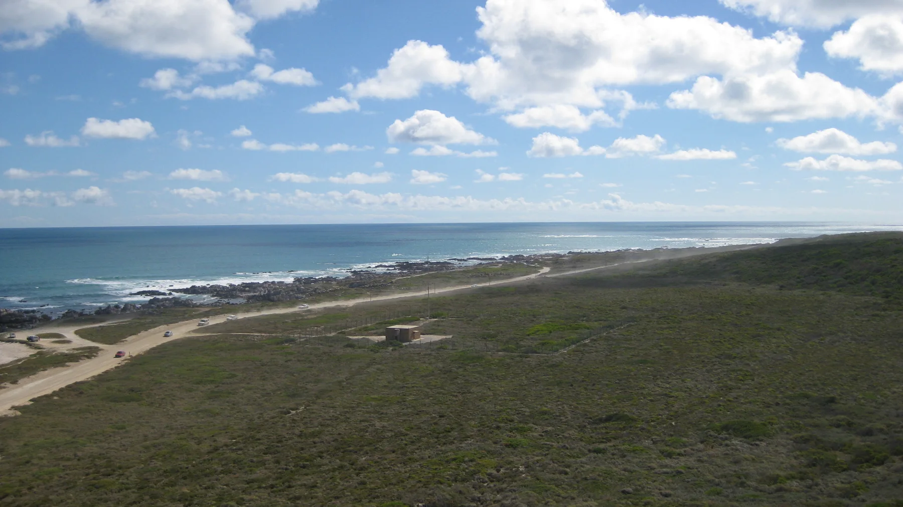 Low green vegetation slopes toward a distant rocky coastline.
