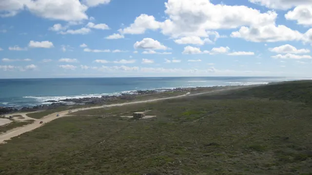 Low green vegetation slopes toward a distant rocky coastline.