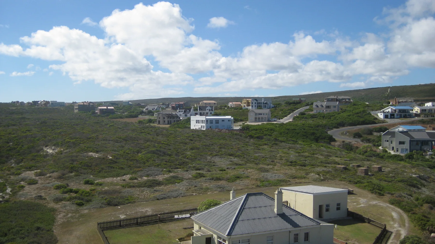 Scattered buildings stand among low coastal shrubs and tracks.