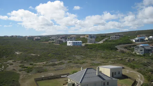 Scattered buildings stand among low coastal shrubs and tracks.