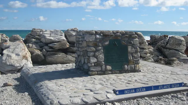 A stone marker stands on a paved platform beside shoreline rocks.