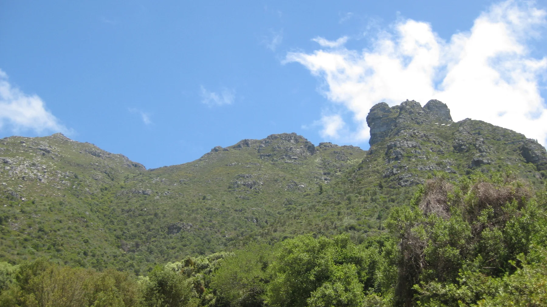 Green mountain slopes form a saddle beneath white clouds.
