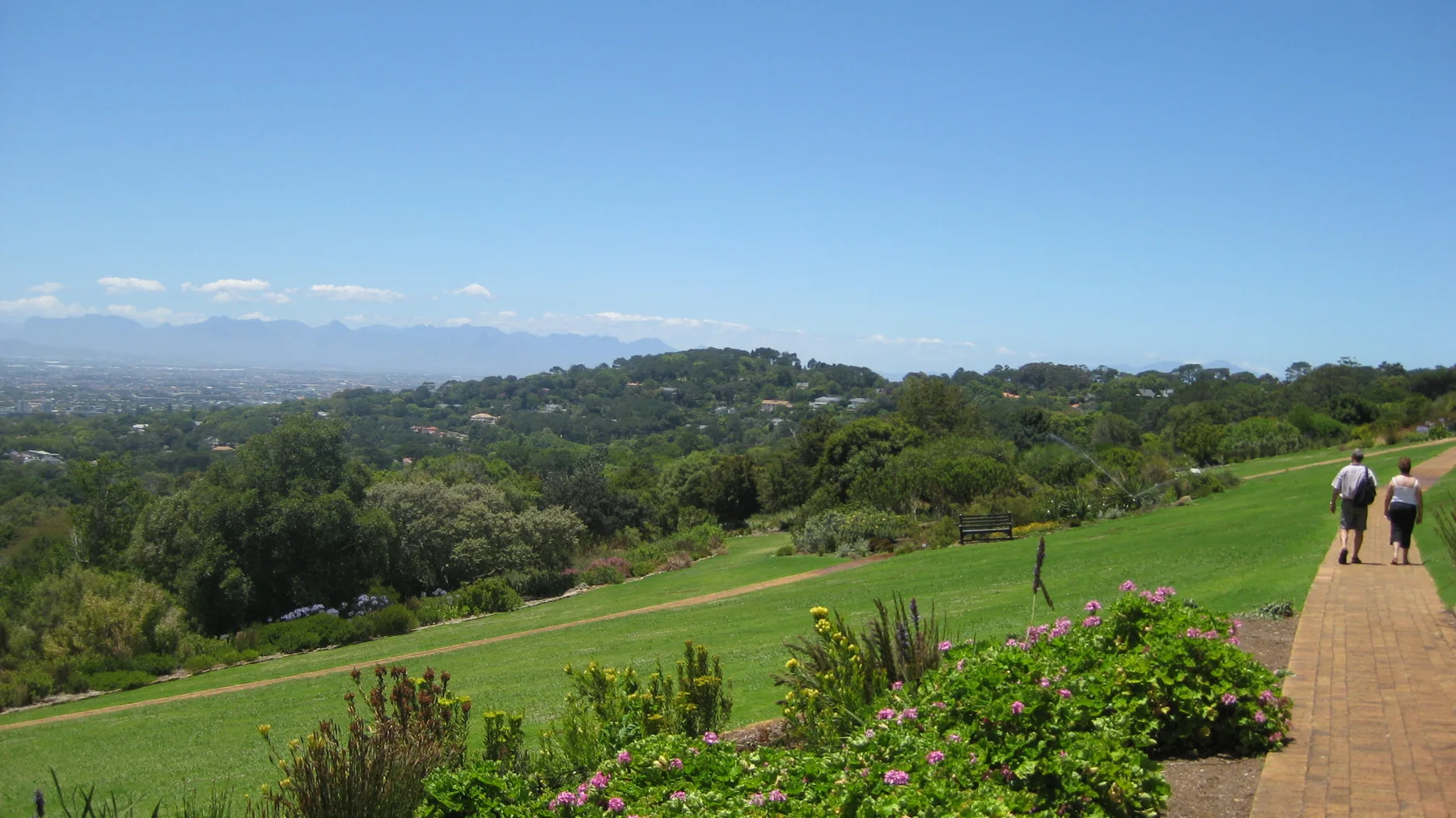 People walk along a path above broad green garden lawns.