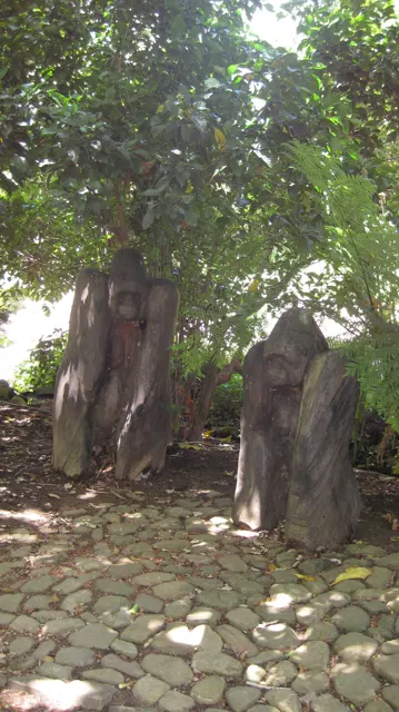 Sculptural forms stand beside a tree on patterned paving.