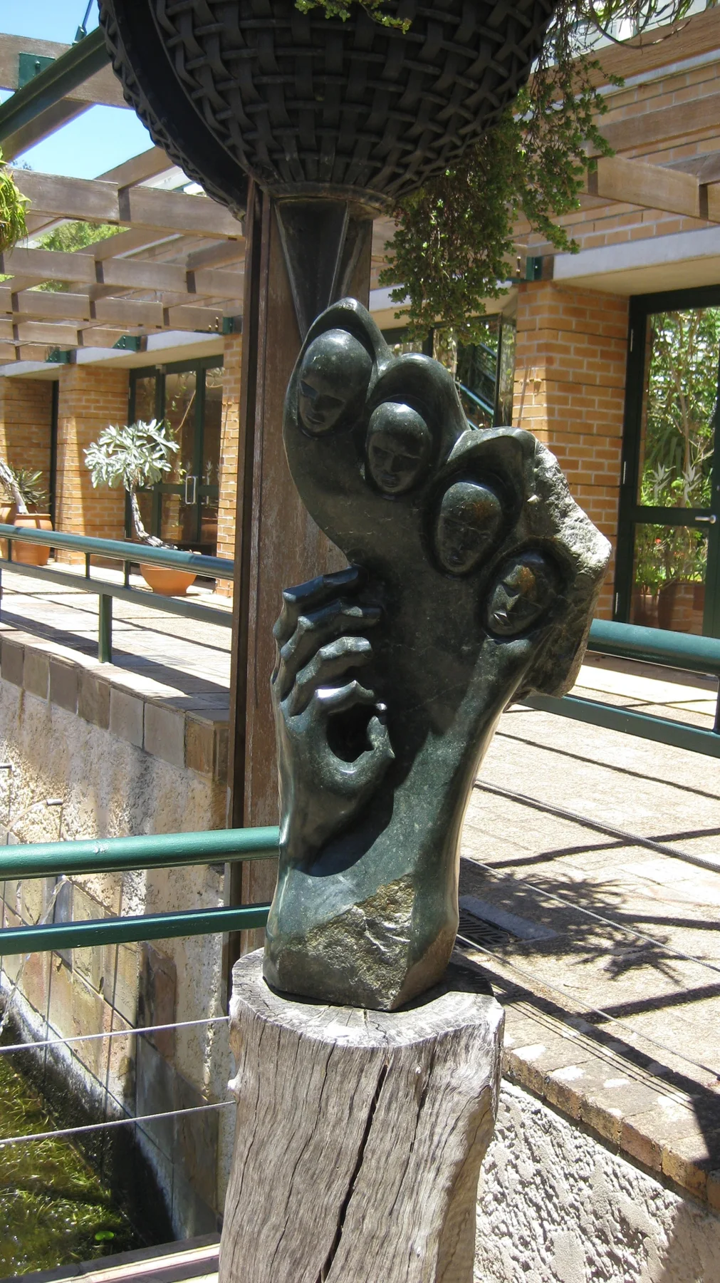 A dark abstract sculpture stands on a pedestal beside glass and railings.