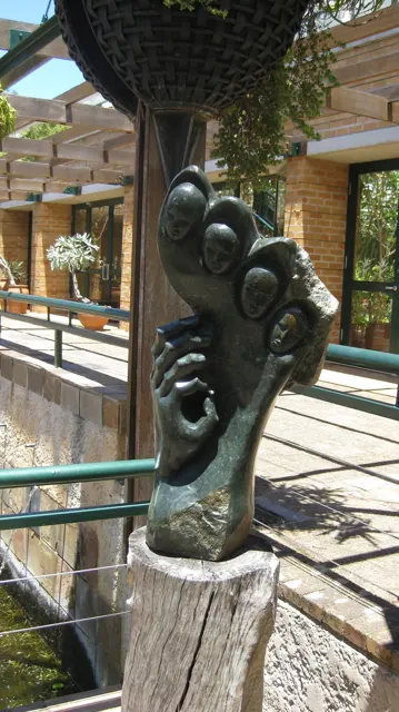 A dark abstract sculpture stands on a pedestal beside glass and railings.