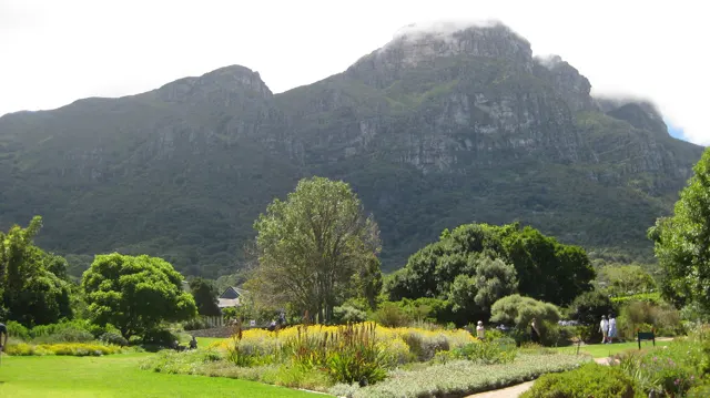 Garden lawns and trees lie beneath a cloud-topped mountain.