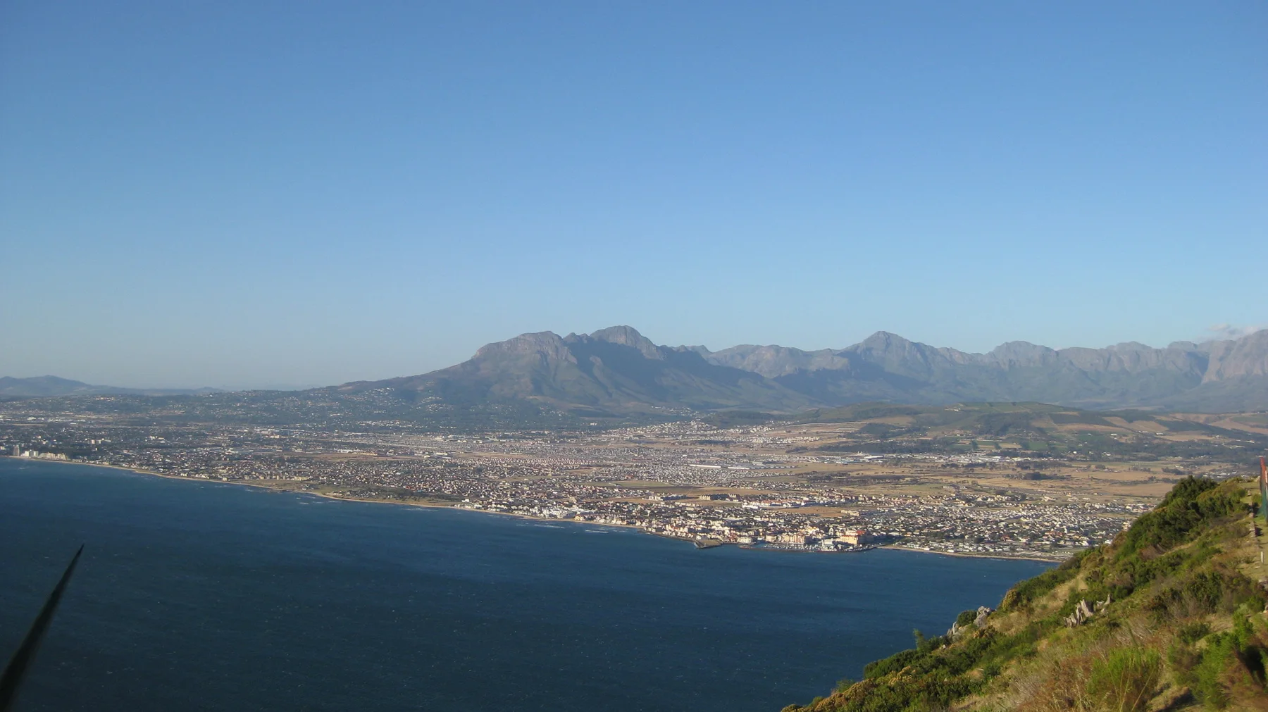 A mountain range rises beyond a long coastal town and bay.