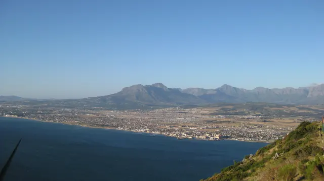 A mountain range rises beyond a long coastal town and bay.