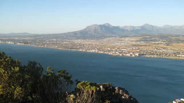 Foreground shrubs frame a developed coastal plain and blue bay.