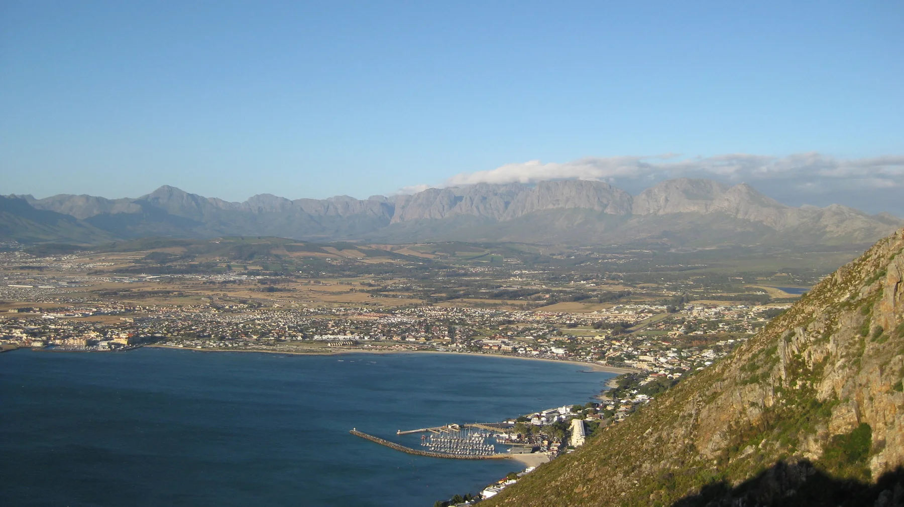 A bay curves beneath a steep foreground slope and distant mountains.