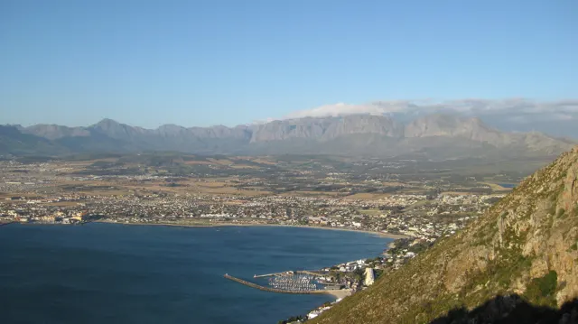 A bay curves beneath a steep foreground slope and distant mountains.