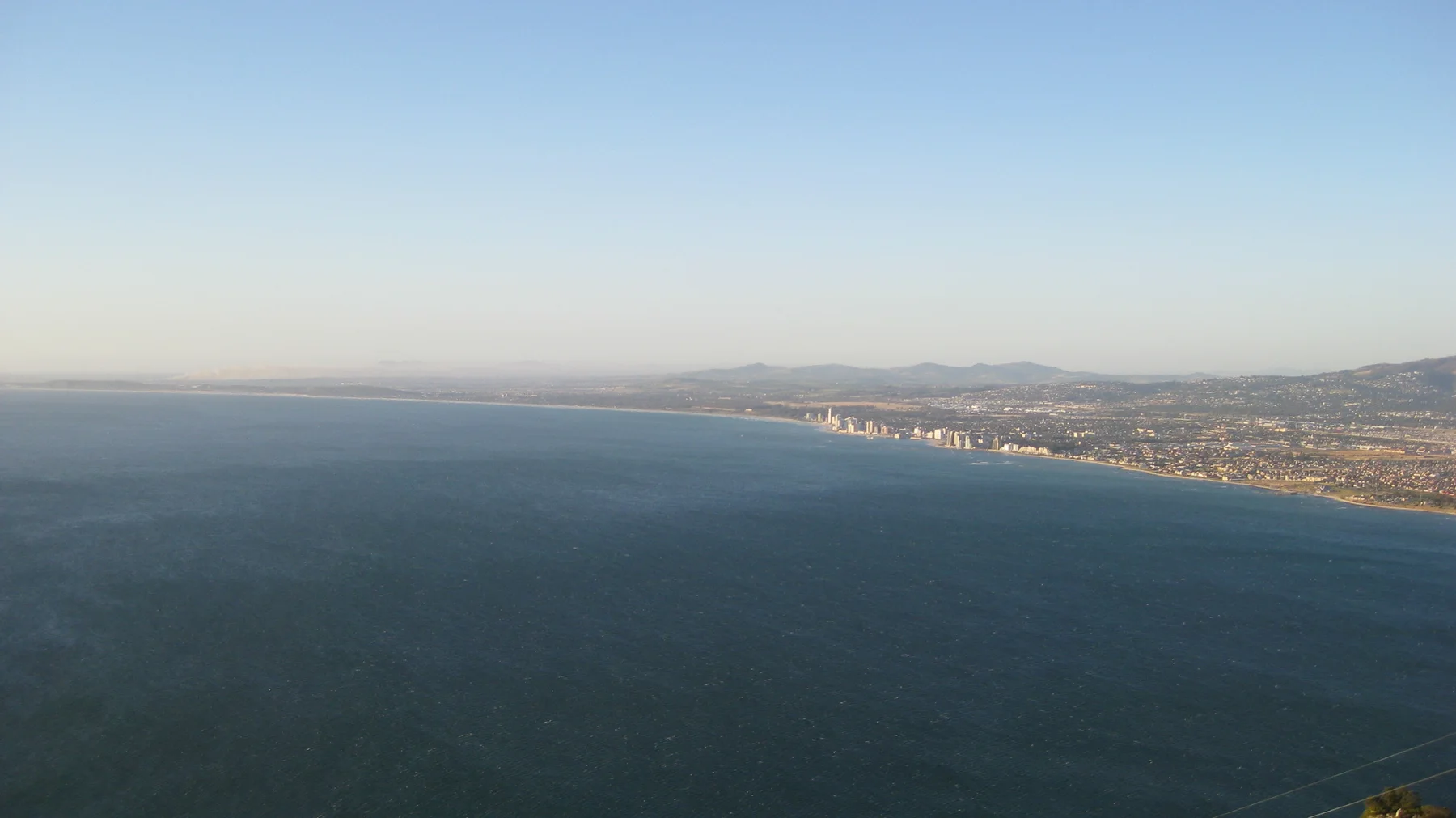 A long line of coastal buildings borders a broad blue bay.