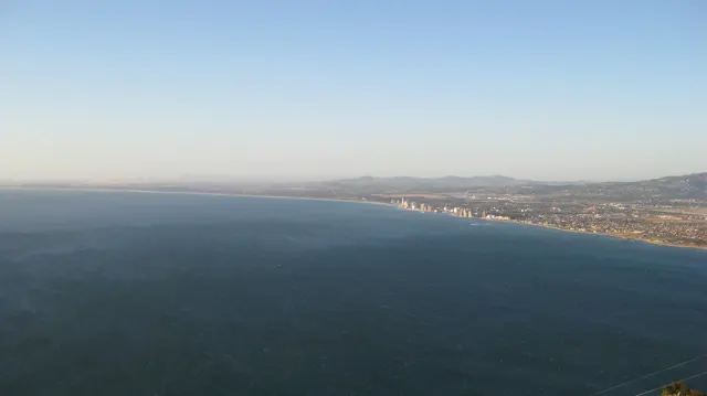 A long line of coastal buildings borders a broad blue bay.