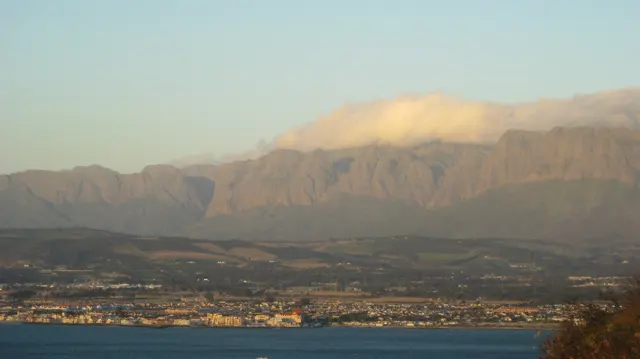 Golden cloud rests on a mountain ridge above a coastal town.