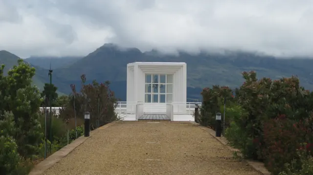 A small white pavilion stands at the end of a gravel path.