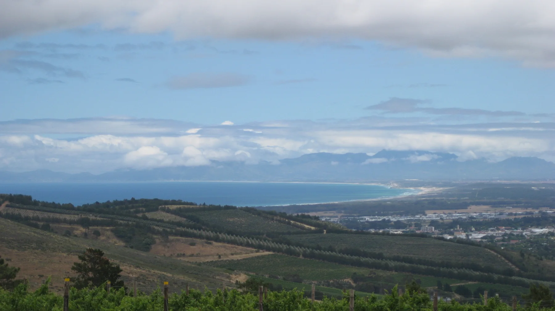 Green valley slopes lead toward a blue coastline beneath layered clouds.