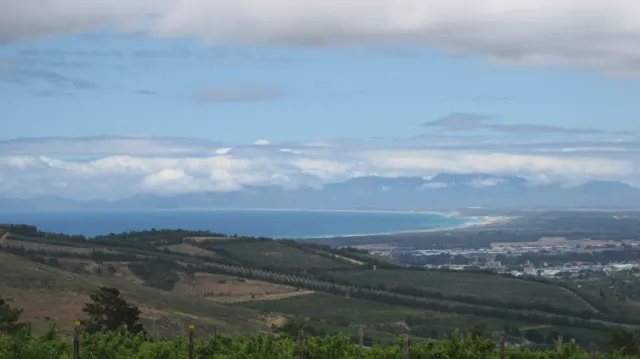 Green valley slopes lead toward a blue coastline beneath layered clouds.