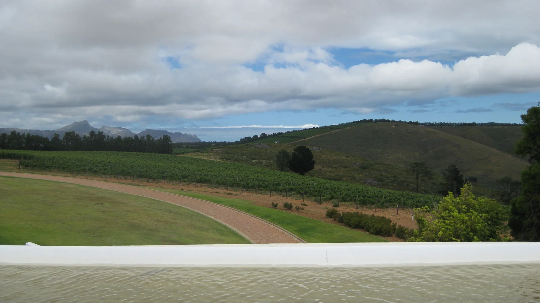 A pale curved path crosses a lawn below cultivated hills.