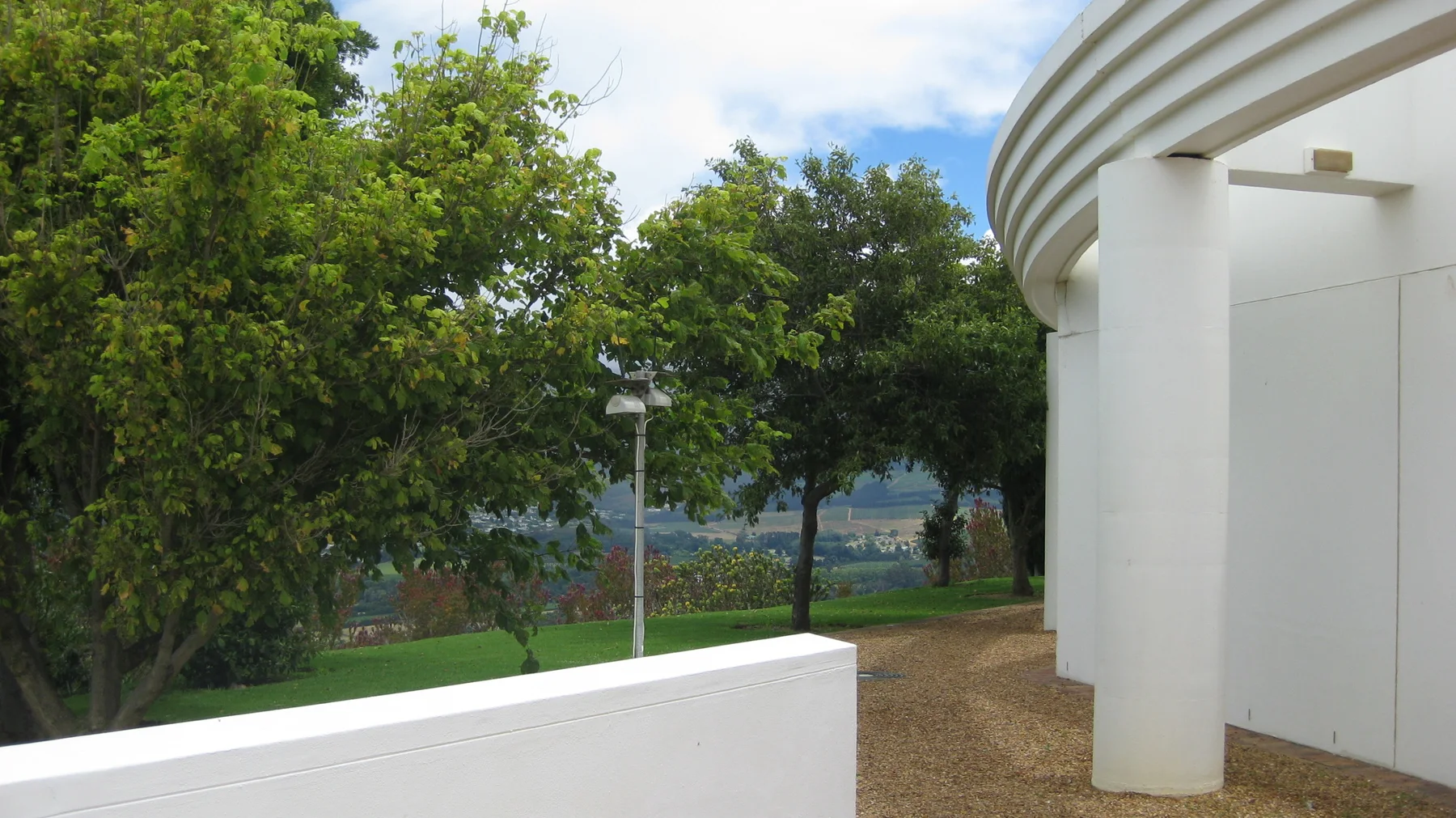 A curved white exterior wall borders trees and a gravel path.