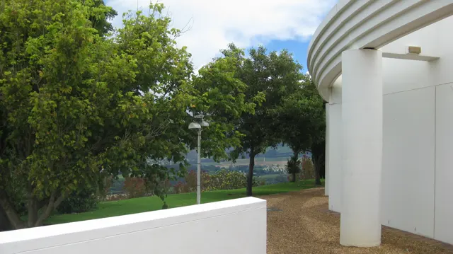 A curved white exterior wall borders trees and a gravel path.