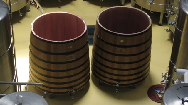 Two large open wooden vats stand among metal winery equipment.