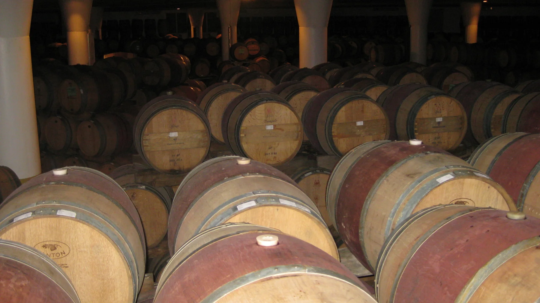 Rows of wooden barrels fill a dimly lit cellar.