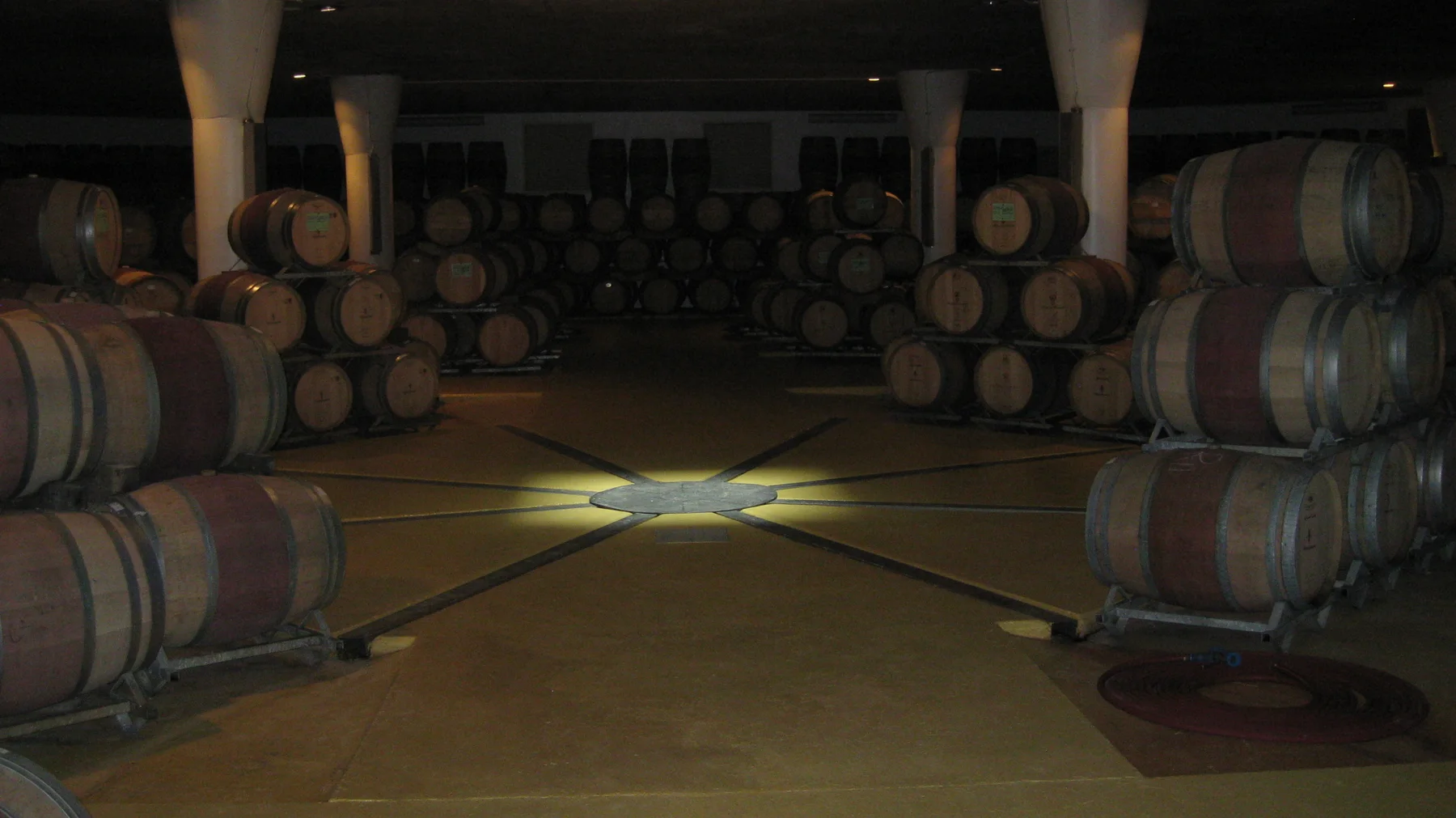 Stacked barrels surround an open cellar floor with a central pattern.