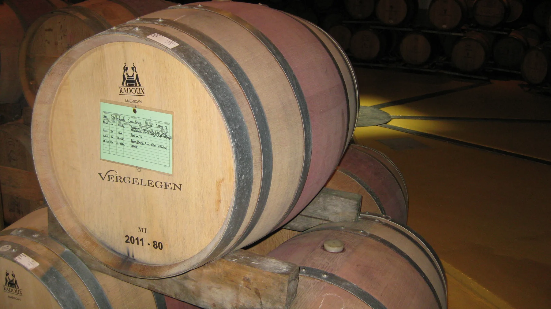 A labeled wooden barrel rests among stacked cellar barrels.