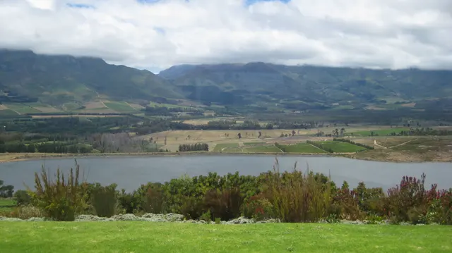 A green lawn borders a reservoir view beneath mountain clouds.