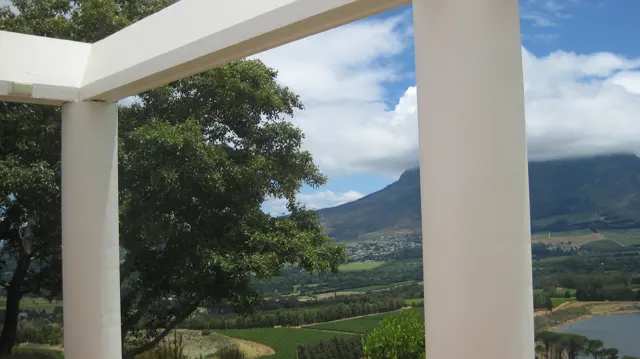 White pergola beams frame a leafy tree and distant valley.