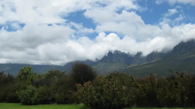 A cloud-covered range rises above trees and cultivated rows.