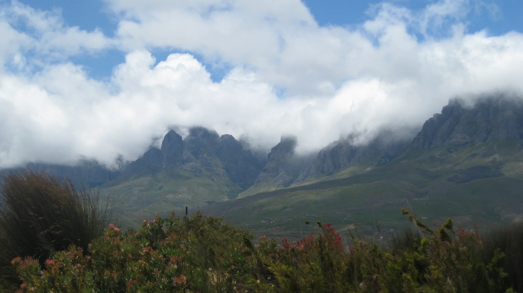 Cloud flows over steep peaks above dark green slopes.